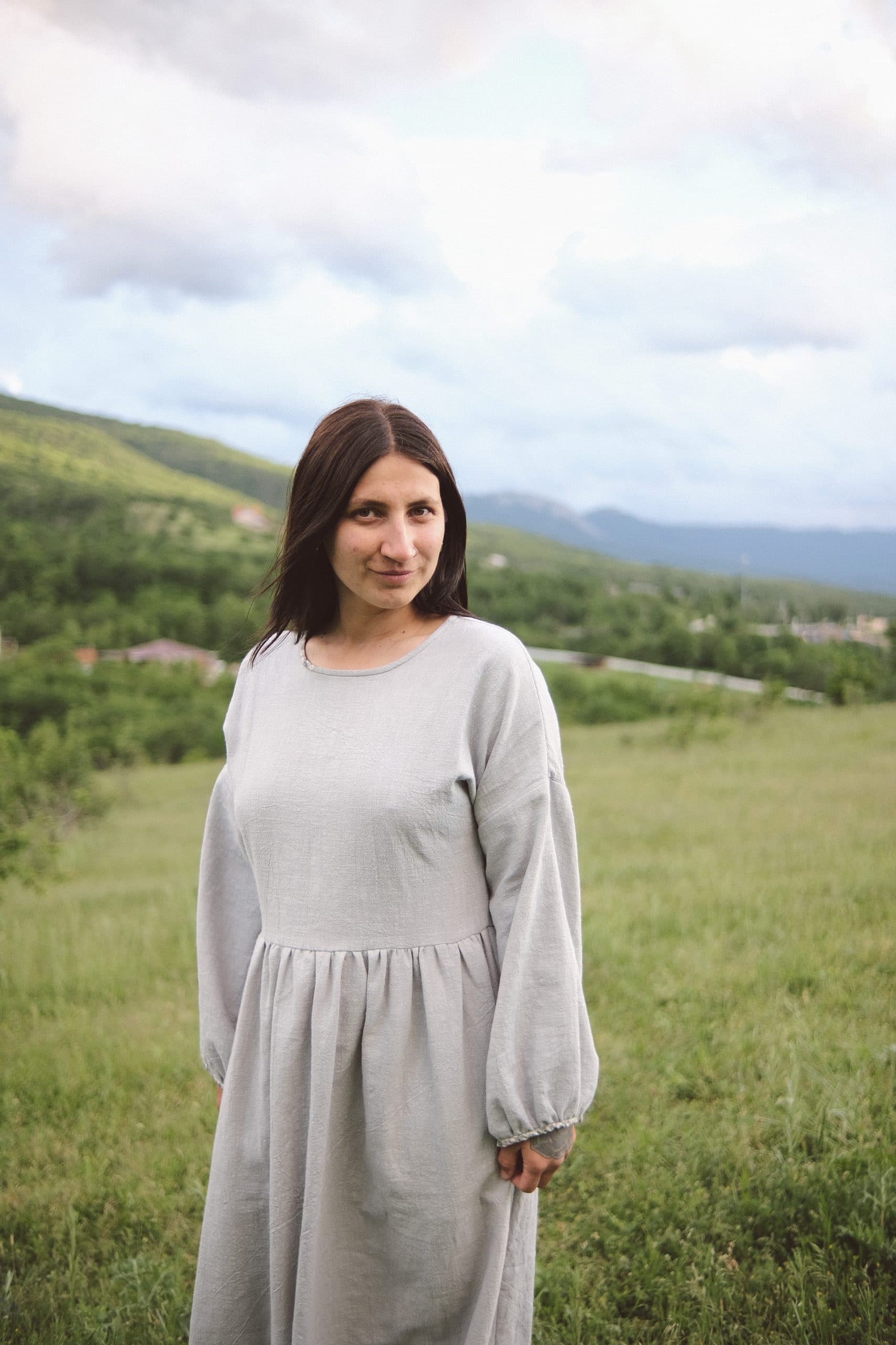 The grey-blue dress from the shoulders down — gathered waist and full sleeves in a meadow