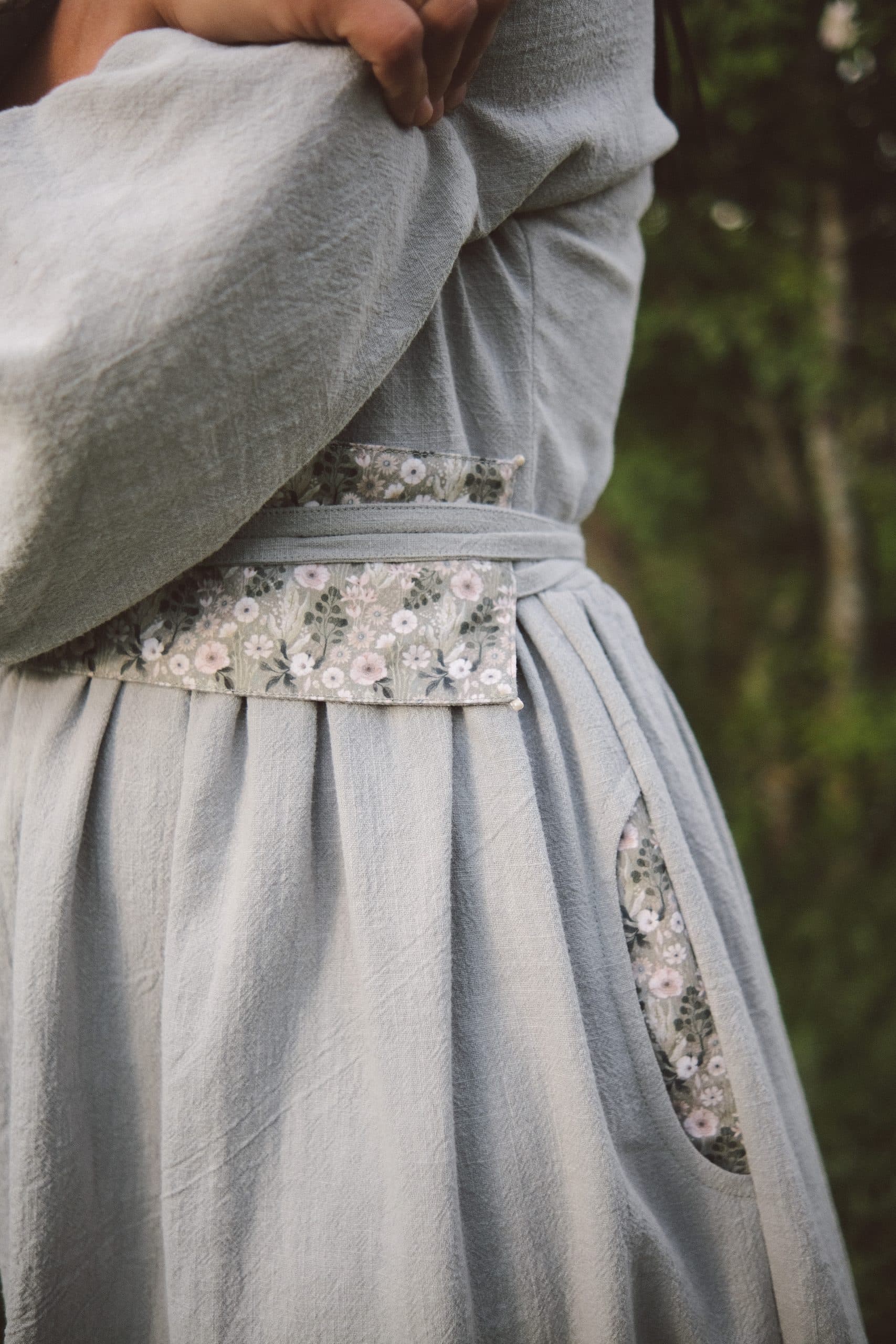 A flowered sash band and flower-lined pocket on a grey-blue dress