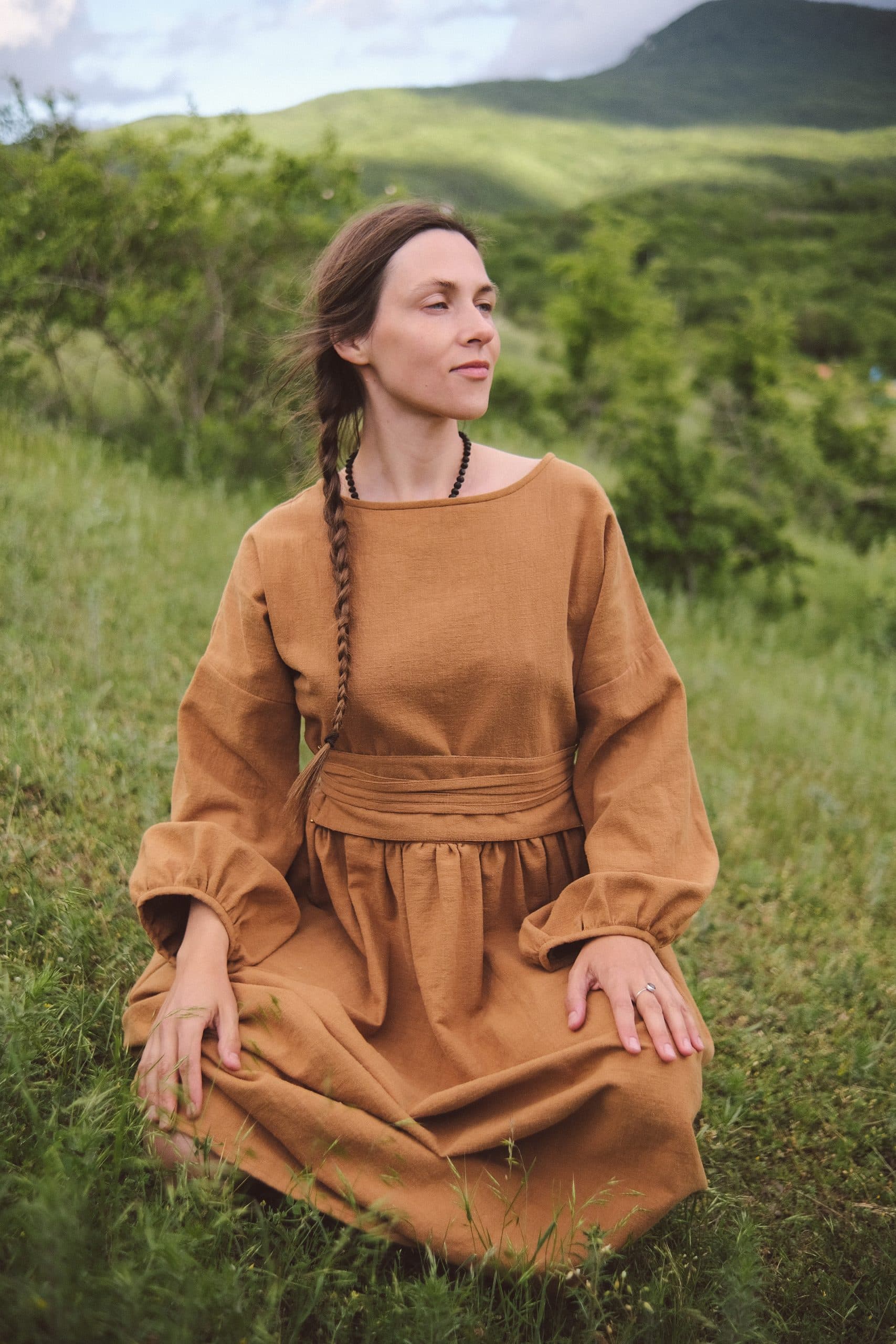 The ochre dress from the waist down — wrapped sash, gathered skirt, hands resting on it