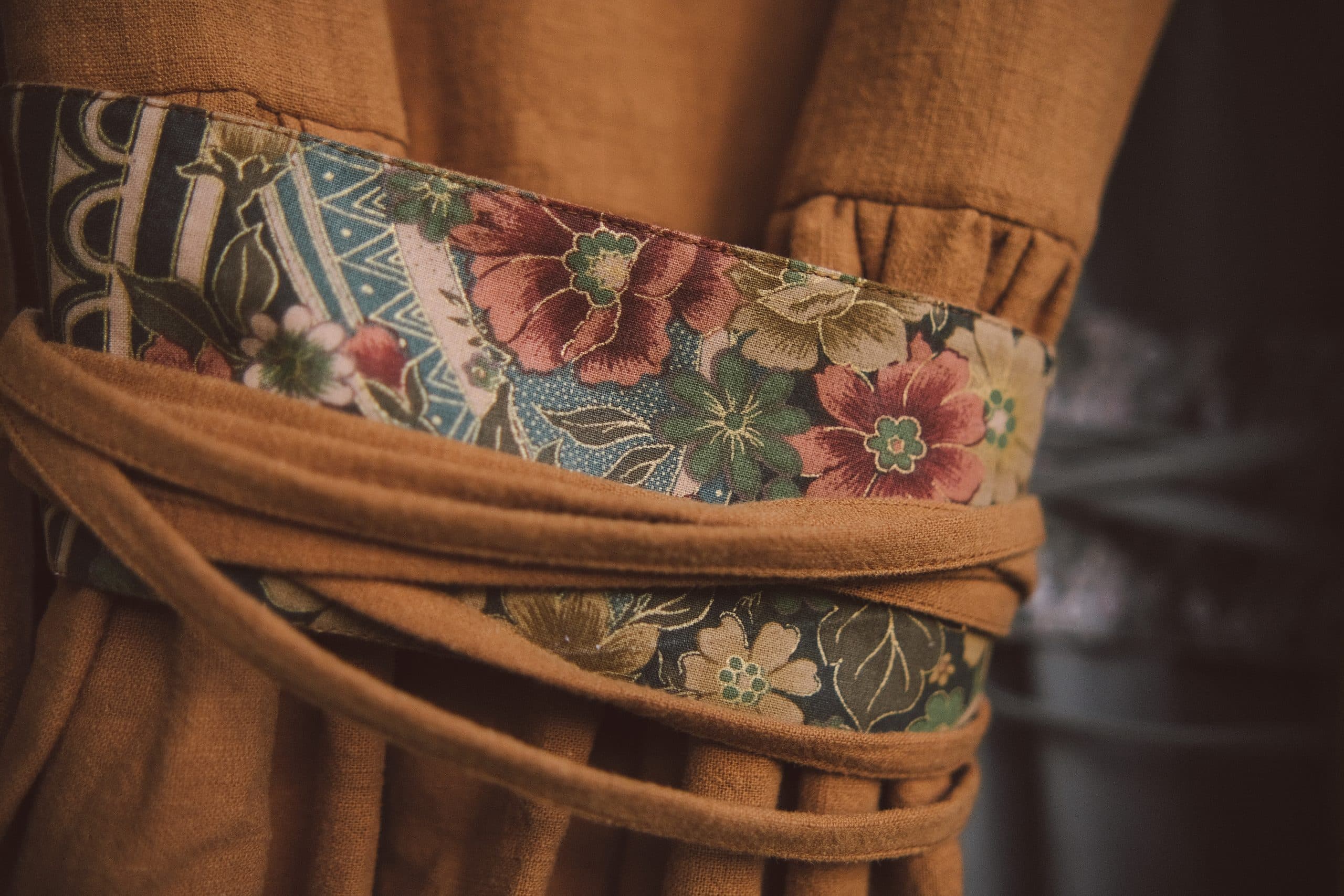 A flowered sash band wrapped and tied over pleated ochre cloth, close