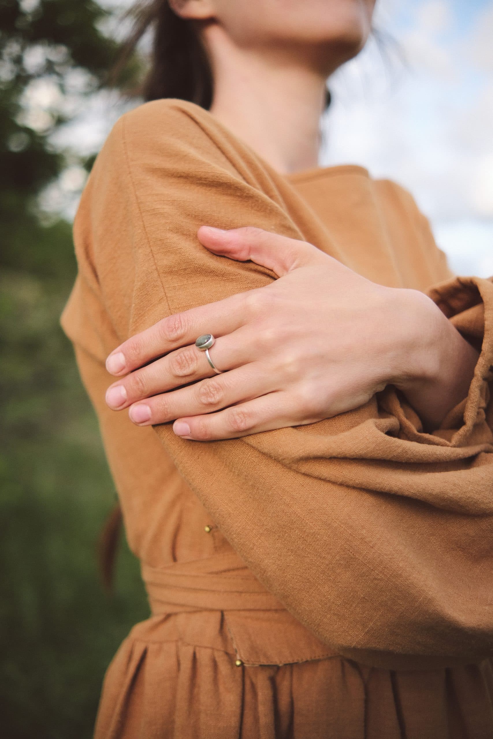 Arms folded across the chest of an ochre dress, a ring on one hand