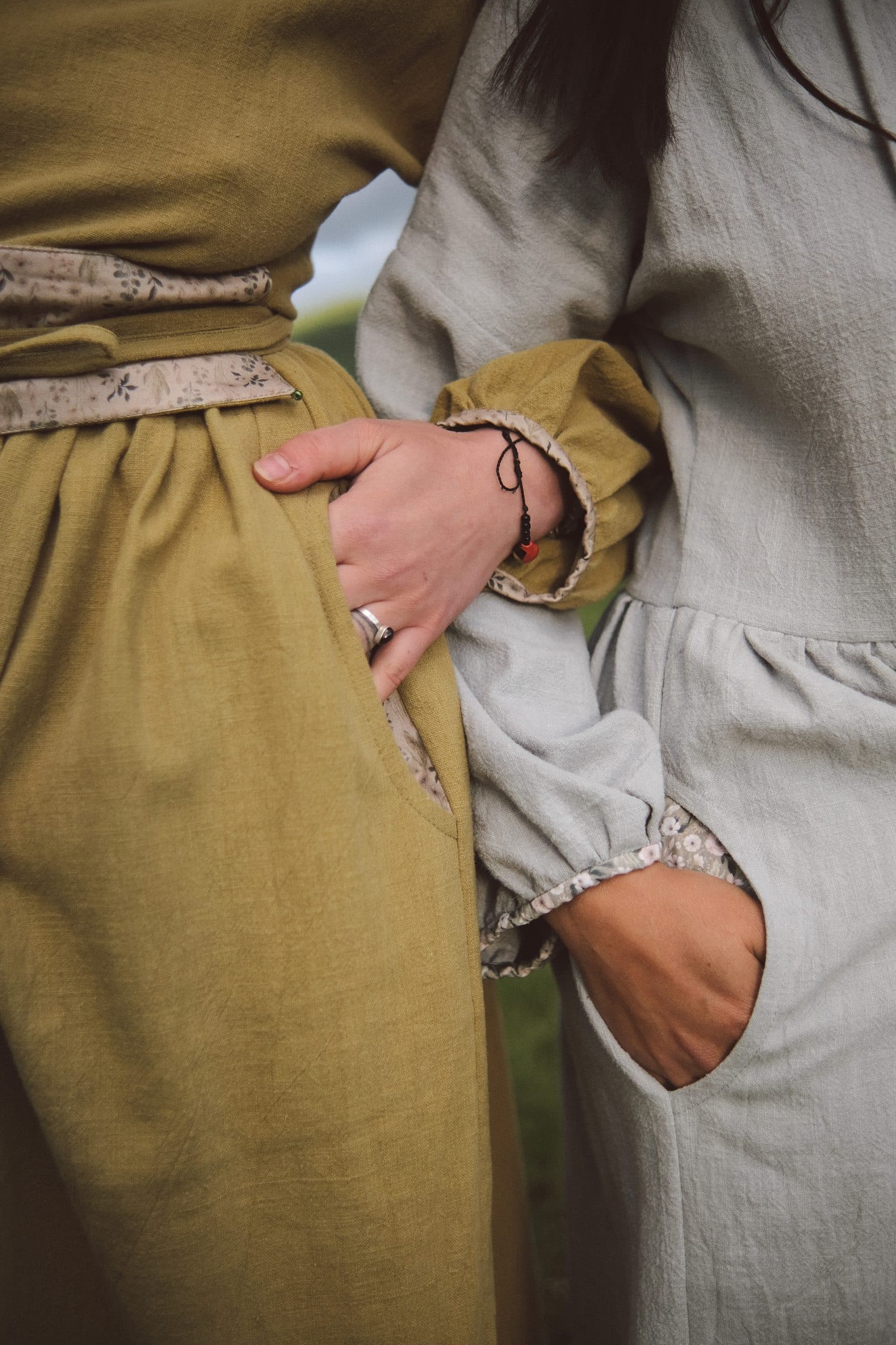 A hand tucked into a friend's pocket, olive and grey-blue cloth side by side